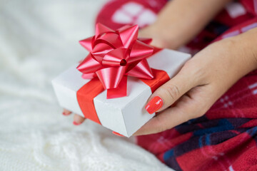 
girl in santa claus pajamas holding a box of surprise gift with a red bow for the holiday christmas and new year