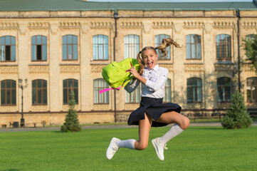 Happy energetic child in formal uniform hold school bag jumping in scholyard, schooling