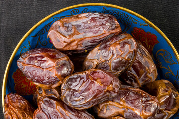 Big luxury dried date fruit in bowls on the dark surface, kurma ramadan kareem concept, close up.