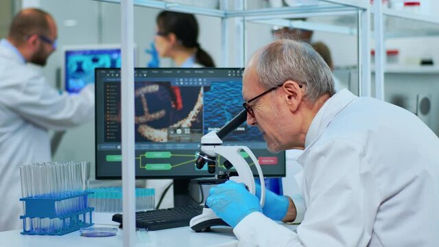 Medical research scientist conducting DNA experiments under microscope in modern equipped laboratory. Multiethnic team examining virus evolution using high tech for vaccine development against covid19