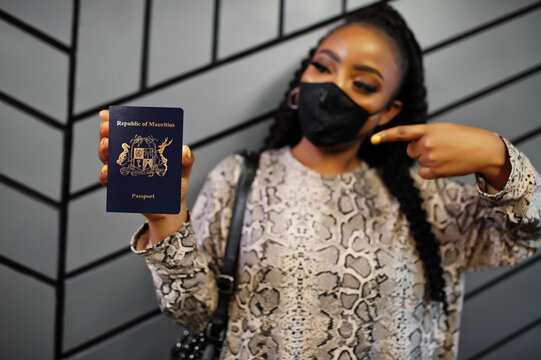 African woman wearing black face mask show Mauritius passport in hand. Coronavirus in Africa country, border closure and quarantine, virus outbreak concept.