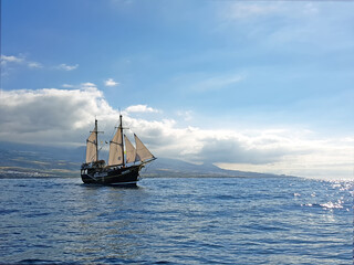 Fototapeta na wymiar Old sail ship in the blue calm sea/ocean with white clouds