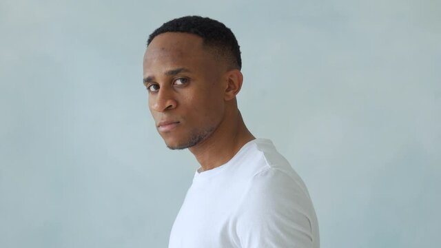 Thinking black Afro American man with serious expression looking with eyes directly into camera while posing against light studio wall. 