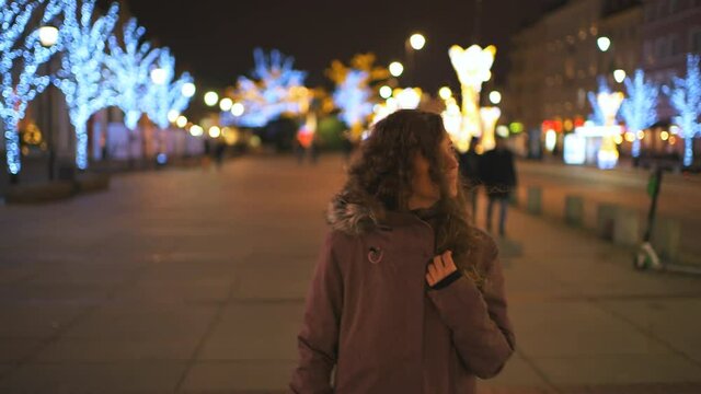 Pov point of view backwards walking young woman in Warsaw, Poland old town at night with Christmas holiday illumination decorations on street illuminated bokeh background in winter