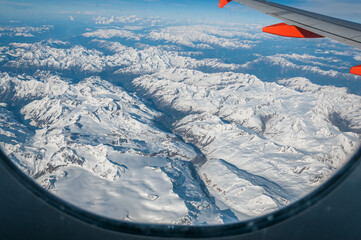 Naklejka na ściany i meble View of the snow-capped Alps from an airliner porthole. Concept: air travel, aerial panoramas. Frame given by the airplane window