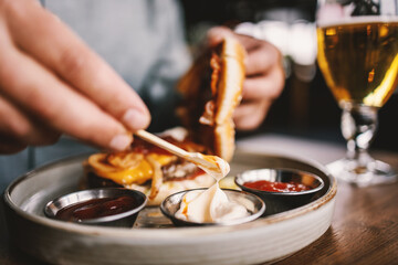 Closeup of man sitting in restaurant and putting mayo in burger.