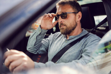 Middle aged bearded man with eyeglasses driving his car.