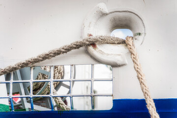 Nautical equipment on a boat. Closeup on two tightropes going through ships side hole from anchor...