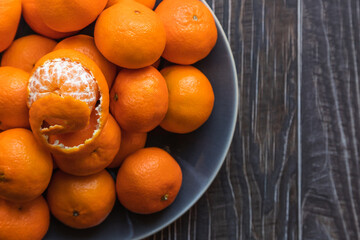 close up on a plate of ripe orange tangerines on a wooden table, one tangerine peeled - 395141022