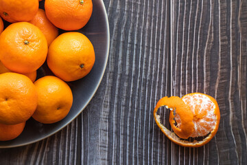 close up on a plate of ripe orange tangerines on a wooden table, one tangerine peeled - 395141613