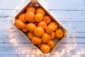 a box of ripe orange tangerines on a wooden table with Christmas lights, giving festive mood - 395141699