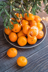 a bowl of ripe orange tangerines on a wooden floor under a Christmas tree, healthy present from Santa - 395142481