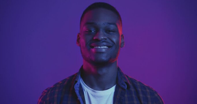 Studio portrait of young handsome african american guy smiling to camera in neon lights