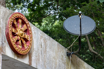 The Dharma Chakra - Wheel of Dharma, symbol of Buddhist with satellite antenna on wall in Buddhist temple, Thailand.