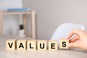 Woman putting cubes with word VALUES on wooden table, closeup