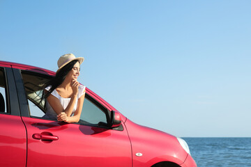 Happy young woman leaning out of car window on beach, space for text. Summer trip