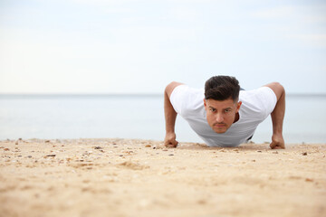 Muscular man doing push up on beach, space for text. Body training