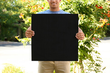 Man holding black empty poster outdoors, closeup. Space for design