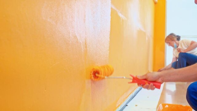 Painting an orange wall with a roller and brush. Man and woman at work doing reforms in the room, house or local business, painter staff. 4k Stock video of professional painting services.