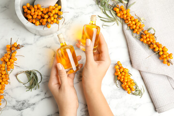 Obraz na płótnie Canvas Woman holding bottles with natural sea buckthorn oil at white marble table, top view