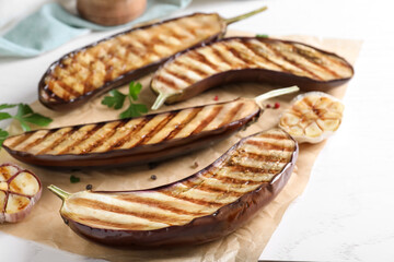 Delicious grilled eggplant halves on white wooden table, closeup