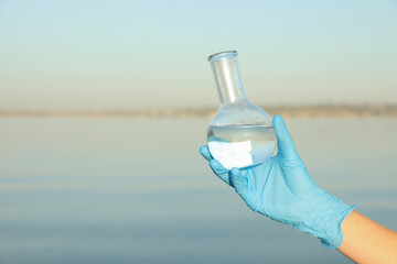 Scientist with florence flask taking sample from river for analysis, closeup