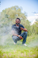 Stylish bearded man exhaling vapor from vape in nature. Electronic cigarette.