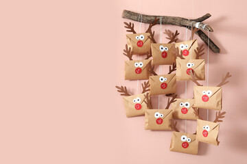 Gifts in envelopes with deer faces hanging on pink wall, space for text. Christmas advent calendar