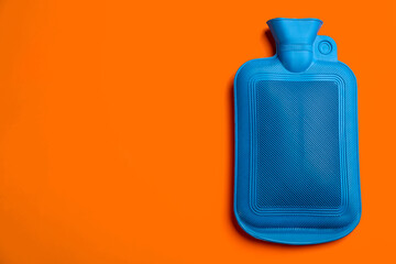 Blue rubber hot water bottle on orange background, top view. Space for text
