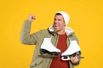 Emotional man with ice skates on yellow background