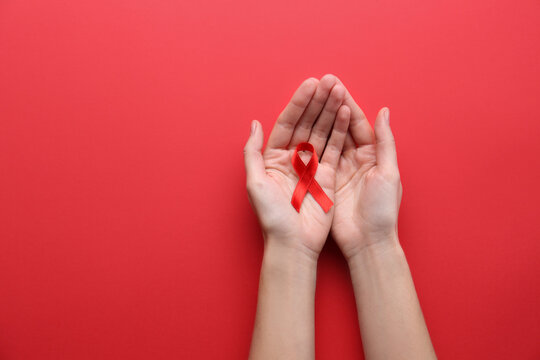 Woman holding red awareness ribbon on color background, top view with space for text. World AIDS disease day