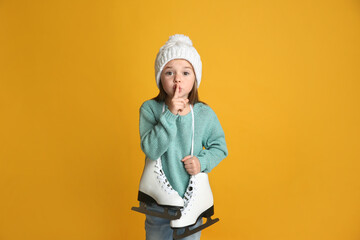 Cute little girl in turquoise knitted sweater with skates on yellow background