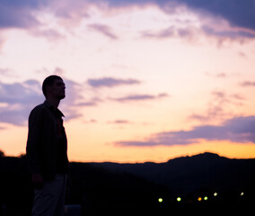 Man silhouette in front of a beautiful purple cloudy sky and orange sun rays 