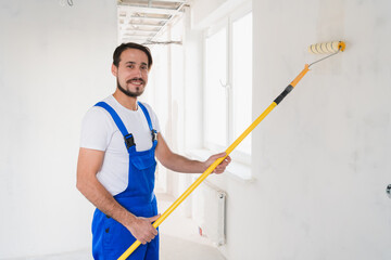Medium shot, general laborer in blue work clothes paints wall in apartment