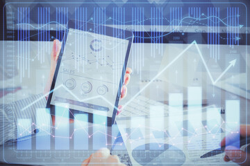 Double exposure of man's hands holding and using a digital device and forex graph drawing. Financial market concept.