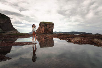 Fototapeta premium Young girl in a rocky landscape at the coast. 