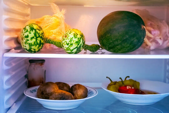 Shelves of an open frige refrigerator with different food, cooked food in pot and plastic container.