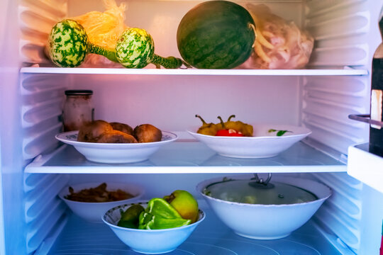 Shelves of an open frige refrigerator with different food, cooked food in pot and plastic container.