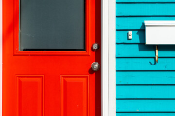 A bright red door with a frosted glass window, silver doorknob and lock. The building is vibrant teal blue colour with a white doorbell and white mailbox or postal box. There's white trim on the door - Powered by Adobe