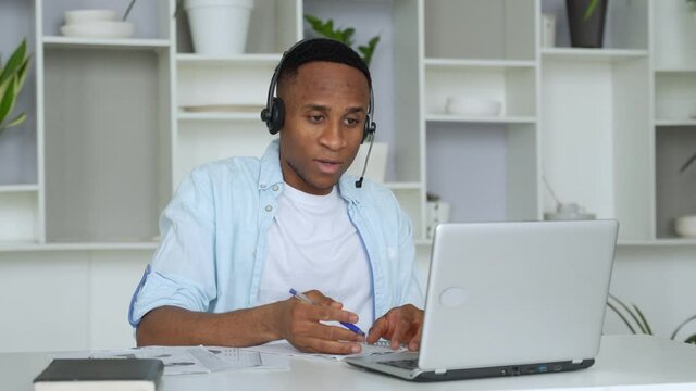 Focused black consultant with a headset looks at a laptop