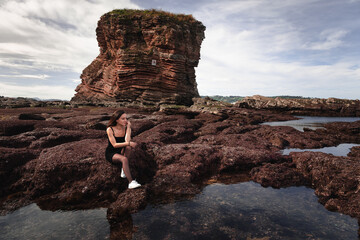 Girl posing with a n elegant black dress at a rocky cove of the basque coast.	
