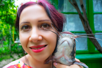 A smiling woman in a pink dress holding a large brown flathead catfish. 