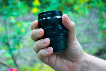 hand holding small camera lens at backyard with green background at sunny day