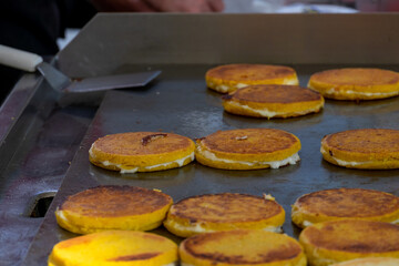 A large frying griddle covered in oil or butter and filled with round golden pancakes or yellow flapjacks and a spatula. The thin yeast dutch pancakes are cooking by a street vendor.  