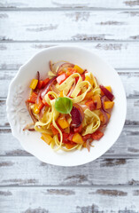 Tagliatelle pasta with pepper, red onion and basil. Bright wooden background. Top view. 