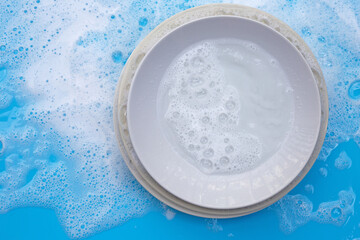 Washing dishes concept. wet blue with soapy foam background.