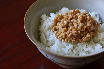 A close up shot of some finely chopped fermented soybeans on freshly cooked white rice in a ceramic rice bowl.