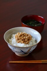 A close up shot of some finely chopped fermented soybeans on freshly cooked white rice in a ceramic rice bowl.