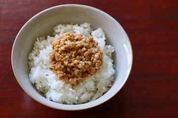 A close up shot of some finely chopped fermented soybeans on freshly cooked white rice in a ceramic rice bowl.