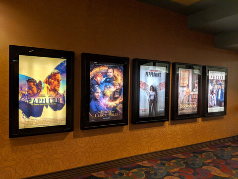Row of movie posters including Papillon, the House with a Clock in it's Wall, Peppermint, The Bookshop, and Puzzle on wall located outside the movie theater
